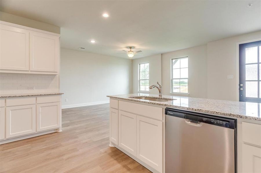 Kitchen with a wealth of natural light, white cabinetry, sink, stainless steel dishwasher, and light wood-type flooring