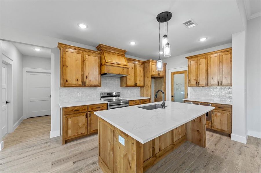 Kitchen featuring decorative backsplash, a kitchen island with sink, premium range hood, and stainless steel electric stove