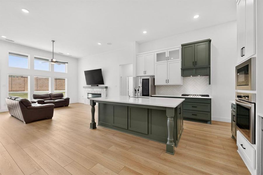 Open-concept living space featuring a central kitchen island with seating, a gas range with a herringbone tile backsplash, integrated stainless steel appliances, wood-finish flooring, and a living area with a fireplace Open-concept living space featuring a central kitchen island with seating, a gas range with a herringbone tile backsplash, integrated stainless steel appliances, wood-finish flooring, and a living area with a fireplace