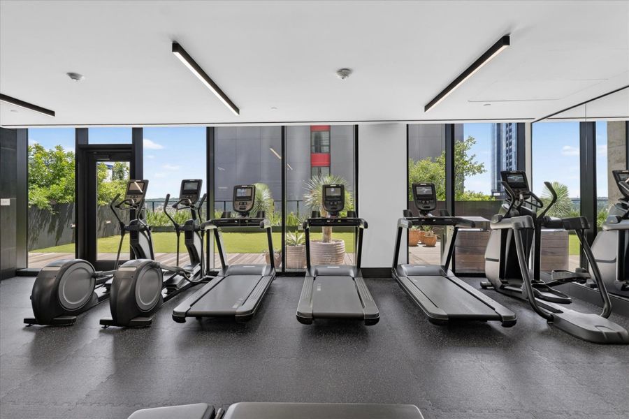 Floor-to-ceiling windows illuminate this well-equipped fitness center, offering views of verdant outdoor spaces.