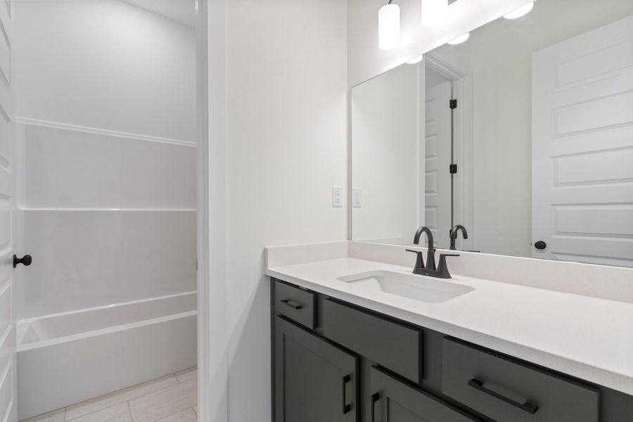 Bathroom vanity featuring dark-toned cabinetry, a stone-composite countertop, an undermount sink, a matte black faucet, and an expansive wall-mounted mirror Bathroom vanity featuring dark-toned cabinetry, a stone-composite countertop, an undermount sink, a matte black faucet, and an expansive wall-mounted mirror