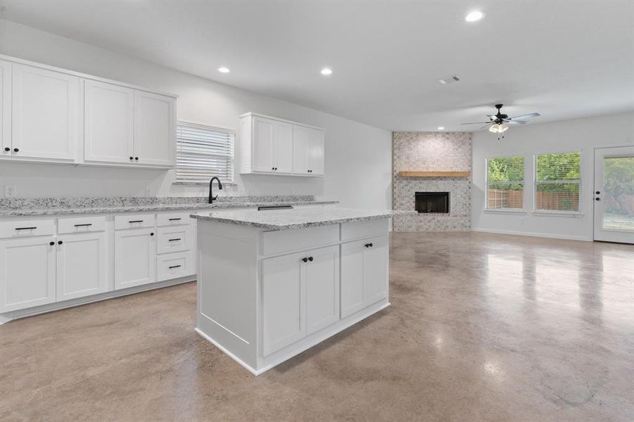 Kitchen featuring a fireplace, light stone counters, white cabinetry, ceiling fan, and a kitchen island