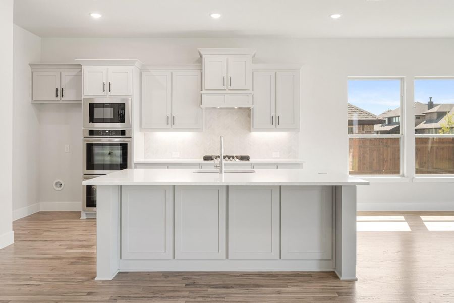 White kitchen with large center island, quartz countertops, stainless steel appliances, and light hardwood floors
