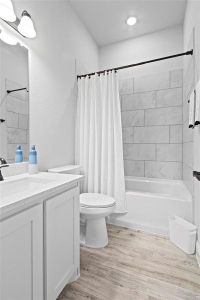 Full bathroom featuring hardwood / wood-style flooring, shower / bath combo with shower curtain, vanity, and toilet