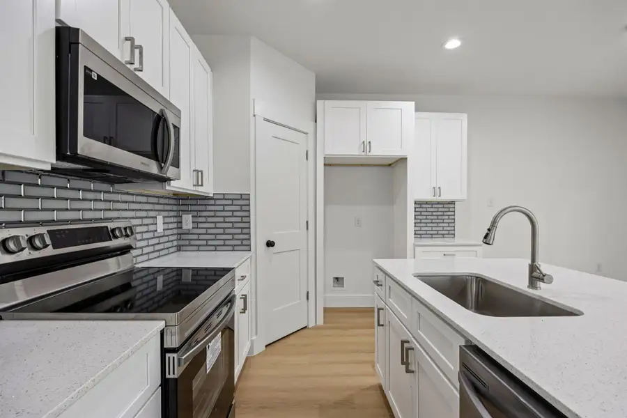 Kitchen with appliances with stainless steel finishes, white cabinetry, light stone counters, light wood finished floors, and recessed lighting Kitchen with appliances with stainless steel finishes, white cabinetry, light stone counters, light wood finished floors, and recessed lighting