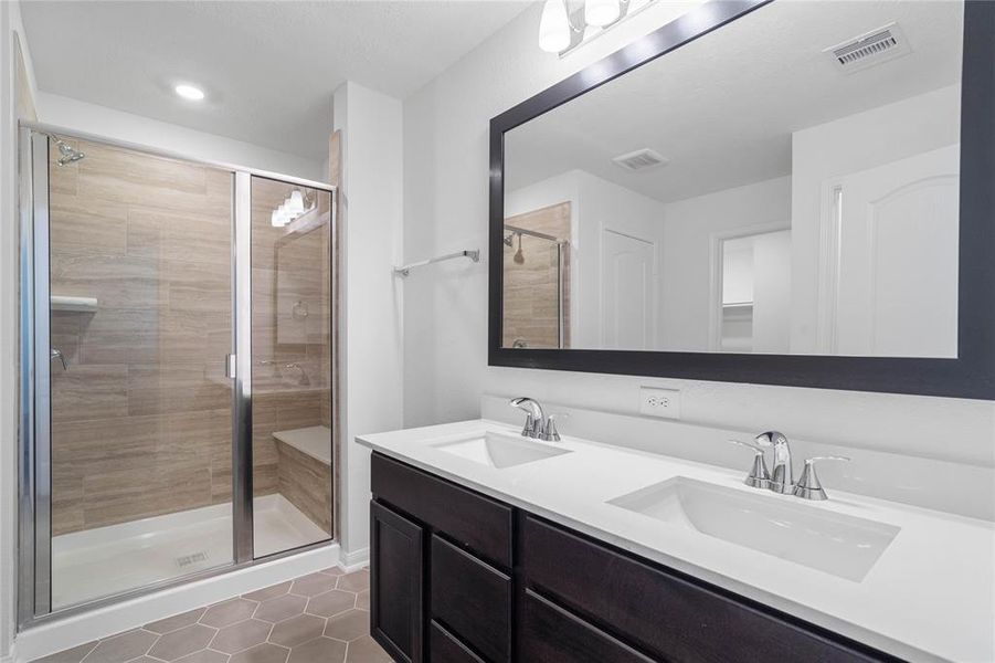 This primary bathroom is definitely move-in ready! Featuring stained cabinets with light countertops and dual vanities, high ceilings, custom paint, wood framed mirror, tile flooring, oversized framed in walk in shower with seat, sleek and dark modern finishes.