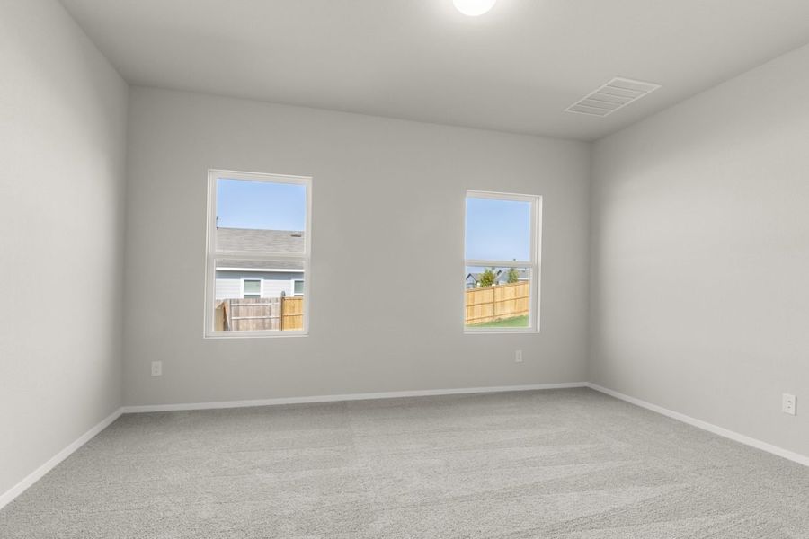 Image of a primary bedroom with tan carpeting, cream walls, windows and white trim