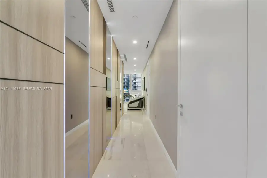 Hallway featuring floor-to-ceiling wood-finish wall paneling, full-length mirror accents, polished tile flooring, and recessed ceiling lighting Hallway featuring floor-to-ceiling wood-finish wall paneling, full-length mirror accents, polished tile flooring, and recessed ceiling lighting