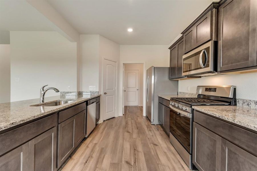 Kitchen featuring stainless steel appliances, light stone counters, light hardwood / wood-style floors, and sink