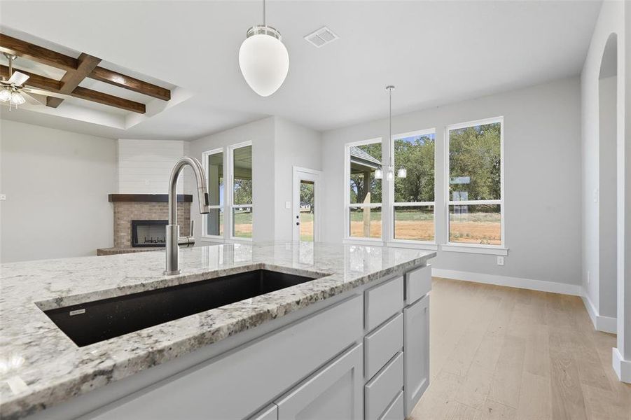 Kitchen featuring coffered ceiling, a fireplace, hanging light fixtures, ceiling fan, and light stone counters