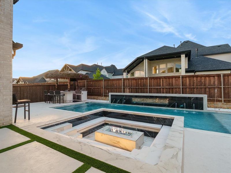 Outdoor living space featuring a multi-level pool with a fire pit, water features, and an outdoor kitchen with a thatched-roof bar Outdoor living space featuring a multi-level pool with a fire pit, water features, and an outdoor kitchen with a thatched-roof bar