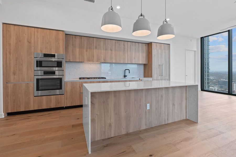 Kitchen featuring light stone counters, modern cabinets, a wall of windows, backsplash, and pendant lighting