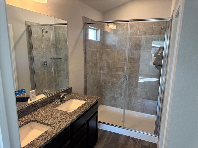 Full bathroom with a textured wall, a stall shower, dark wood-style flooring, and double vanity Full bathroom with a textured wall, a stall shower, dark wood-style flooring, and double vanity