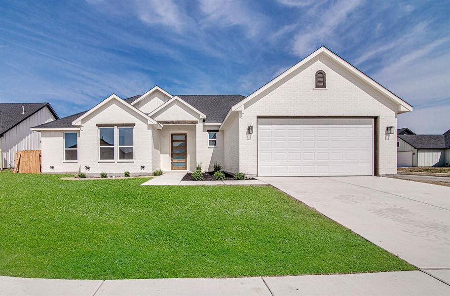 View of front of house with concrete driveway, brick siding, a front yard, a garage, and roof with shingles