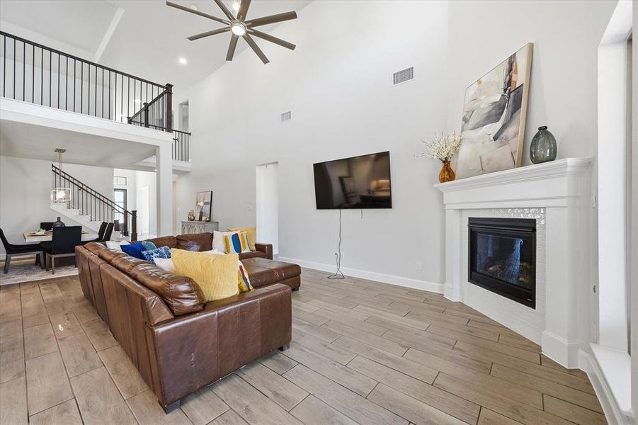 Living area featuring wood tiled floors, ceiling fan, a tiled fireplace, and a high ceiling