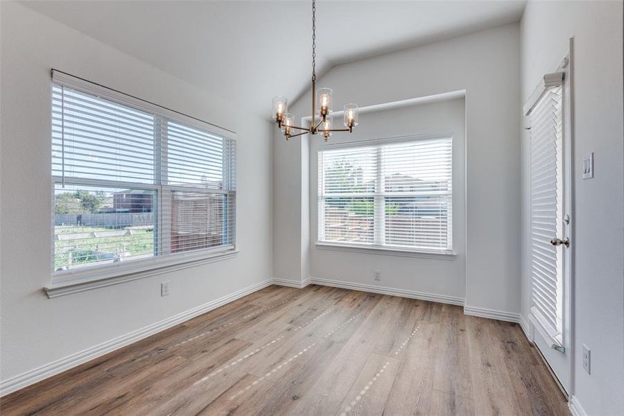 Unfurnished room featuring a wealth of natural light, a chandelier, vaulted ceiling, and light wood-type flooring