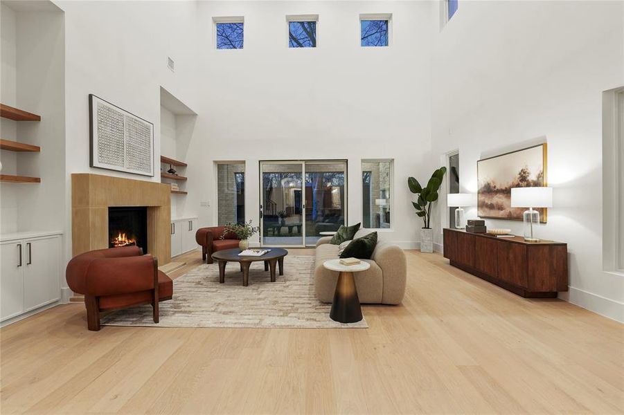 Living room with built in shelves, a lit fireplace, light wood-style flooring, and a high ceiling