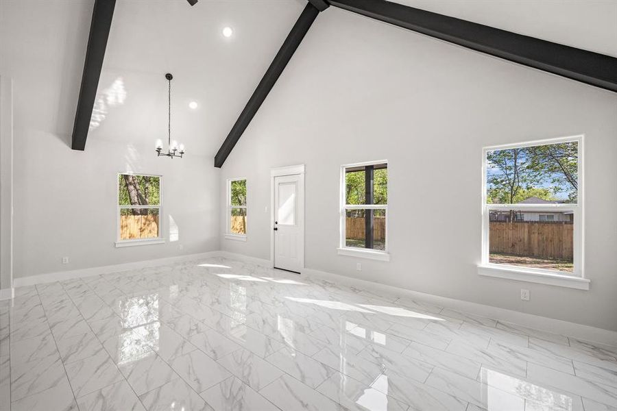 Unfurnished living room with a chandelier, lofted ceiling, and light marble finish flooring