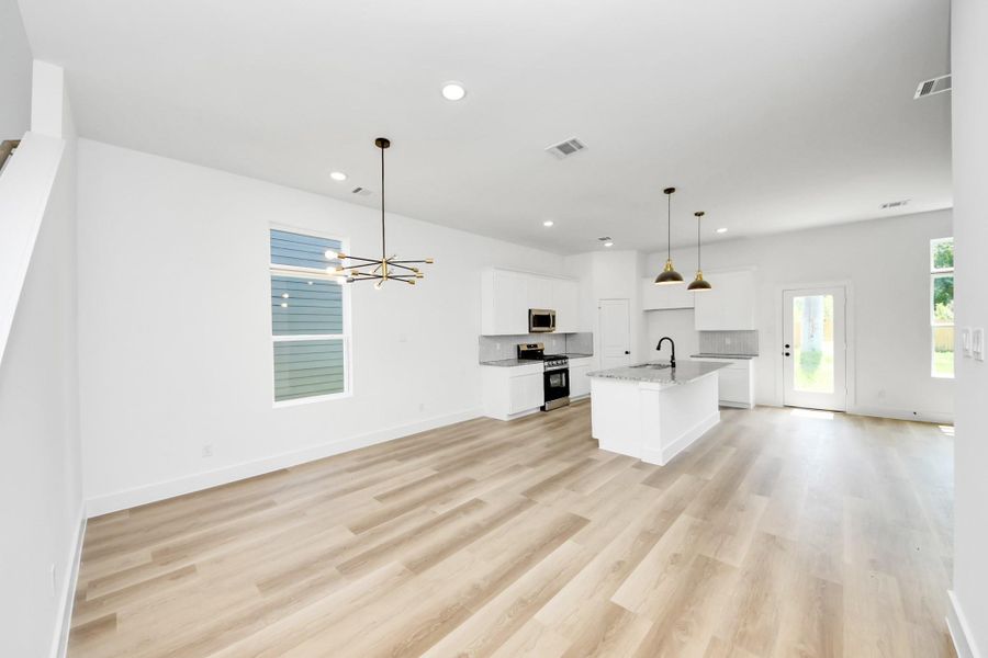 Open-Concept Living & Kitchen – Bright, spacious main living area featuring wood-look flooring, modern lighting, white cabinetry, granite countertops, and a functional kitchen island.