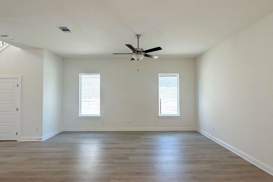 Spacious room featuring wood-finish flooring, two windows with blinds, a ceiling fan, and a five-panel interior door