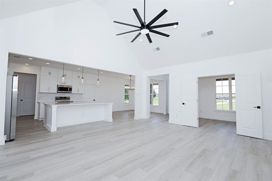 Unfurnished living room with high vaulted ceiling, ceiling fan, light wood finished floors, a chandelier, and healthy amount of natural light