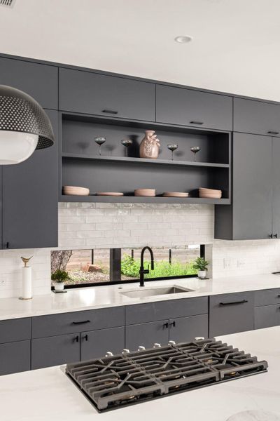 A sleek, contemporary kitchen with dark cabinetry, white countertops, and a unique horizontal window above the sink. A sleek, contemporary kitchen with dark cabinetry, white countertops, and a unique horizontal window above the sink.