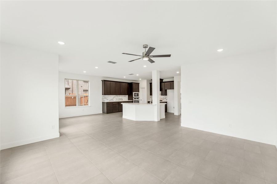 Open living area with tile floors and ceiling fan flowing into kitchen with dark cabinets and white island Open living area with tile floors and ceiling fan flowing into kitchen with dark cabinets and white island