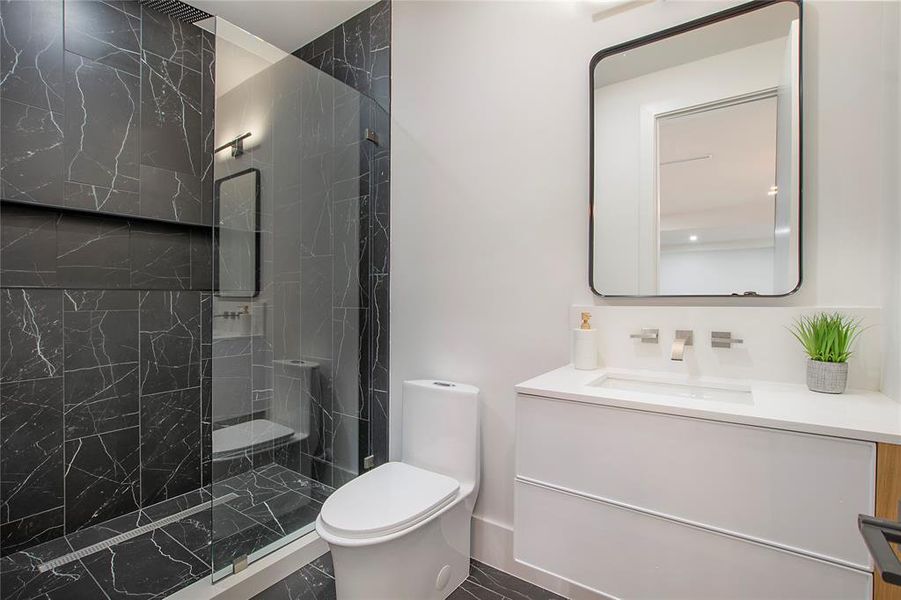 Bathroom featuring a tile shower, vanity, and toilet