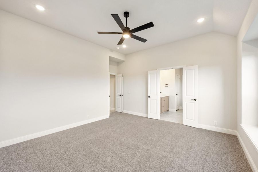 Empty master bedroom with gray carpet, black ceiling fan, and open ensuite bathroom door Empty master bedroom with gray carpet, black ceiling fan, and open ensuite bathroom door