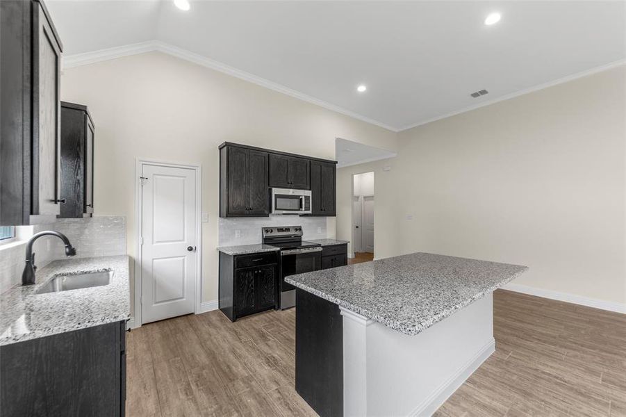 Kitchen featuring a central island with a granite countertop, dark wood-finish cabinetry, stainless steel appliances, and wood-finish flooring