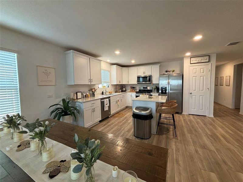 Kitchen featuring stainless steel appliances, white cabinets, a breakfast bar area, light wood finished floors, and recessed lighting