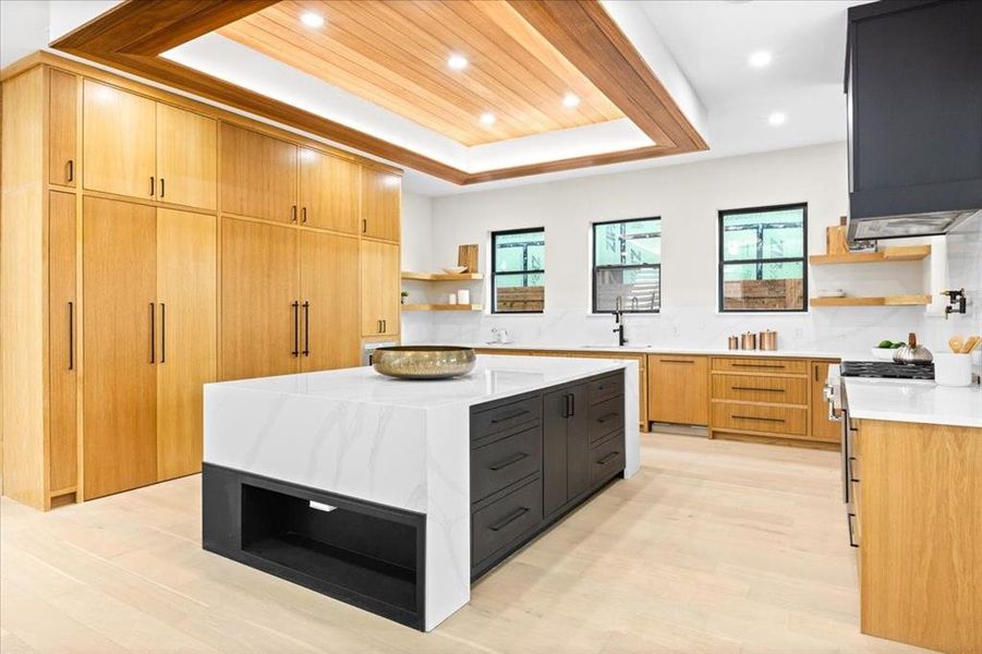 Kitchen featuring light wood-type flooring, high end range, a center island, a raised ceiling, and backsplash