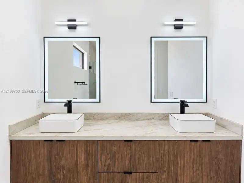 Dual vanity featuring a stone countertop, square vessel sinks, matte black widespread faucets, and integrated LED-backlit mirrors with linear wall-mounted lighting