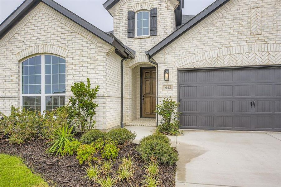 Property entrance featuring brick siding, an attached garage, and concrete driveway