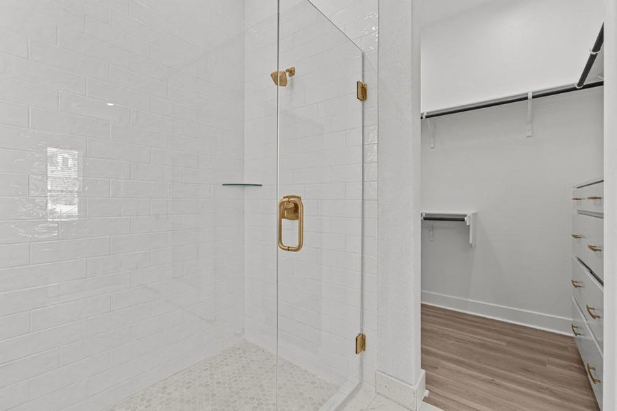 Bathroom with a walk in closet, a shower stall, and light wood-type flooring
