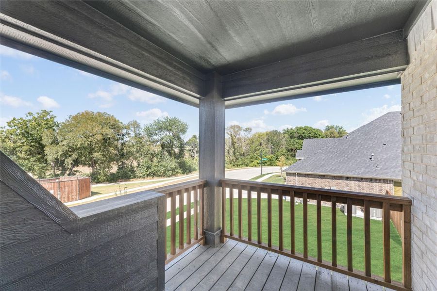 Covered second-floor balcony with wood railing and views of green lawn and trees Covered second-floor balcony with wood railing and views of green lawn and trees