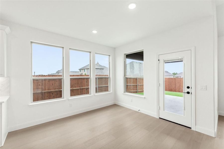Bright empty room with light wood floors, multiple windows, and a glass back door to the yard Bright empty room with light wood floors, multiple windows, and a glass back door to the yard