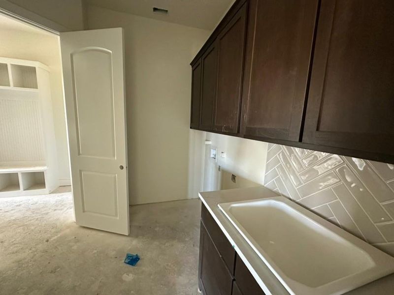 Utility room featuring dark wood-finish cabinetry, a light-toned countertop with an integrated sink, and a herringbone-patterned tile backsplash