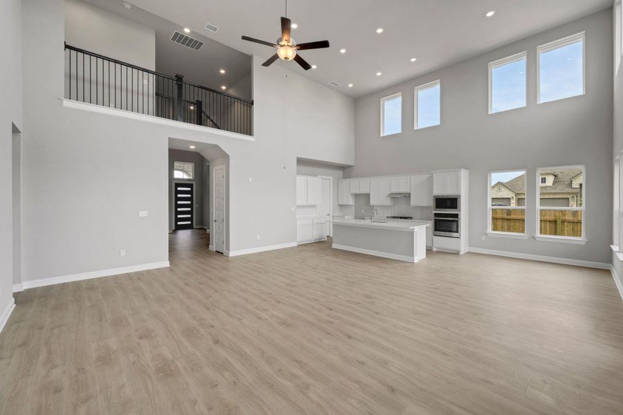 Unfurnished living room with light wood finished floors, ceiling fan, arched walkways, recessed lighting, and a towering ceiling Unfurnished living room with light wood finished floors, ceiling fan, arched walkways, recessed lighting, and a towering ceiling