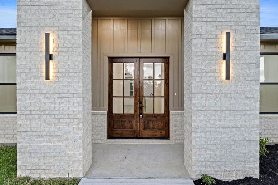 This photo showcases a modern home entrance with elegant double wooden doors framed by light-colored brick. Sleek wall sconces provide stylish lighting, creating an inviting and contemporary facade. This photo showcases a modern home entrance with elegant double wooden doors framed by light-colored brick. Sleek wall sconces provide stylish lighting, creating an inviting and contemporary facade.