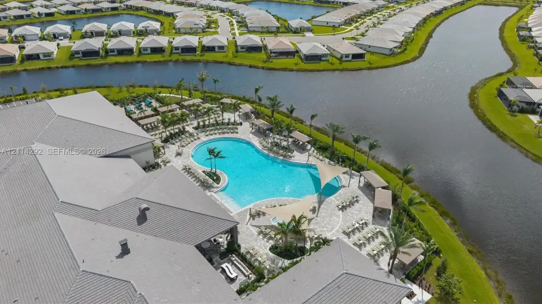 Aerial perspective of a community facility featuring a resort-style swimming pool, paver-stone pool deck, shade structures, and waterfront positioning