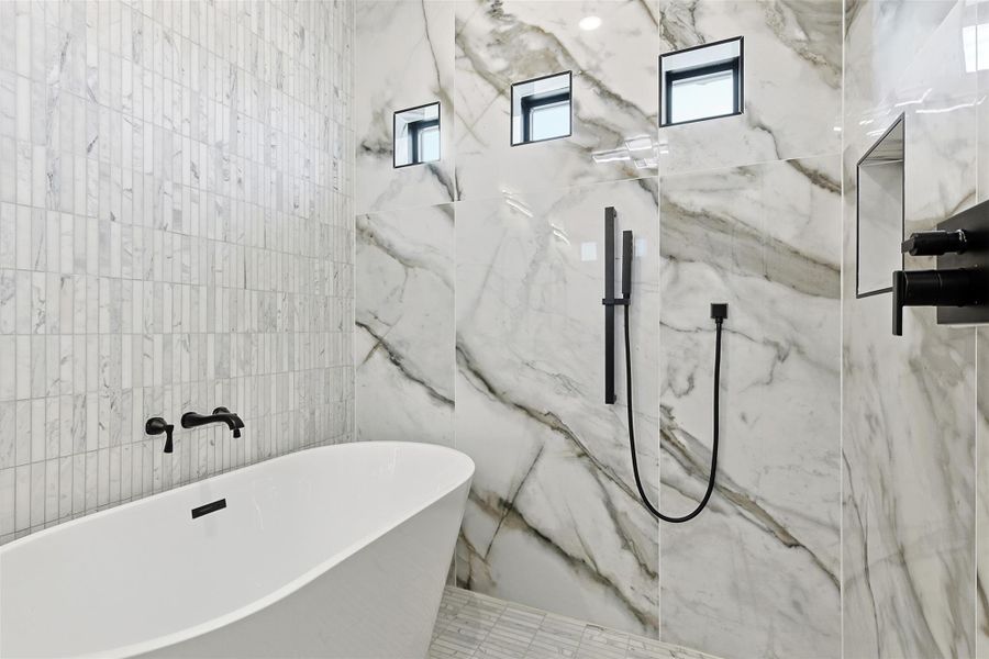 A standalone soaking tub is paired with matte black wall-mounted fixtures and marble-look tile walls.