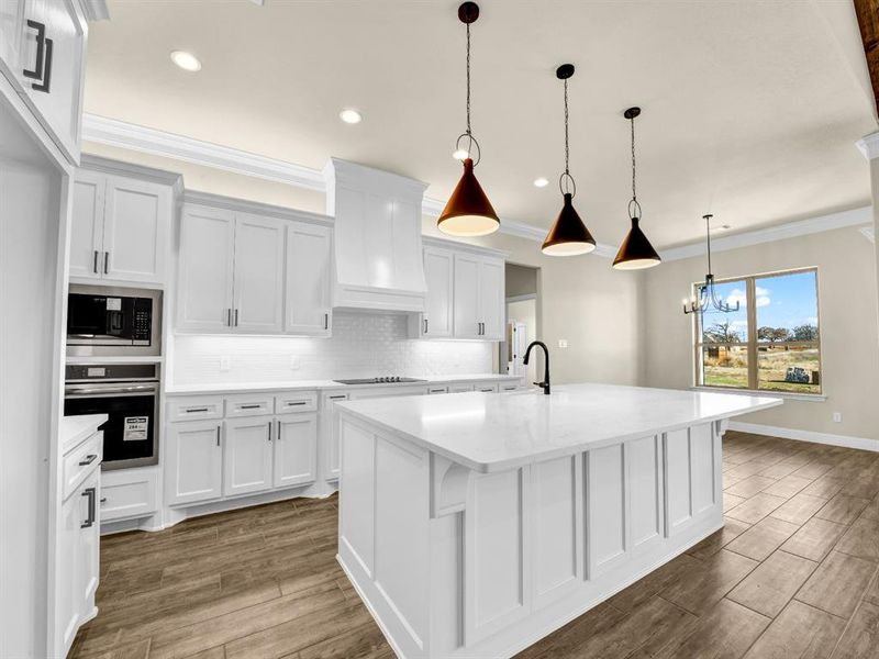 Kitchen featuring stainless steel oven, pendant lighting, a center island with sink, built in microwave, and white cabinets