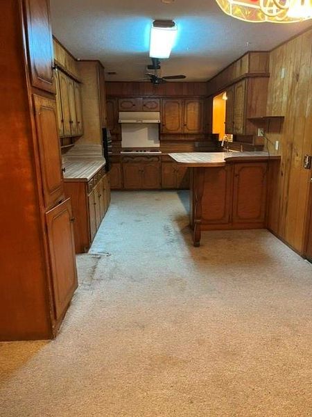 Kitchen featuring wood paneling, extensive cabinetry, a built-in range with hood, a bar-height counter, and ceiling-mounted lighting Kitchen featuring wood paneling, extensive cabinetry, a built-in range with hood, a bar-height counter, and ceiling-mounted lighting