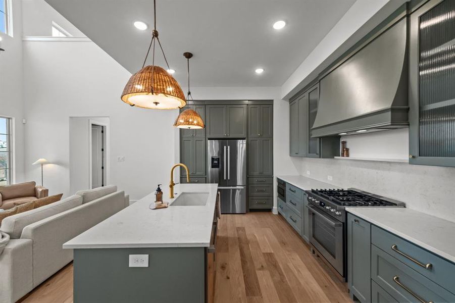 Kitchen featuring appliances with stainless steel finishes, sink, custom exhaust hood, hanging light fixtures, and a kitchen island with sink