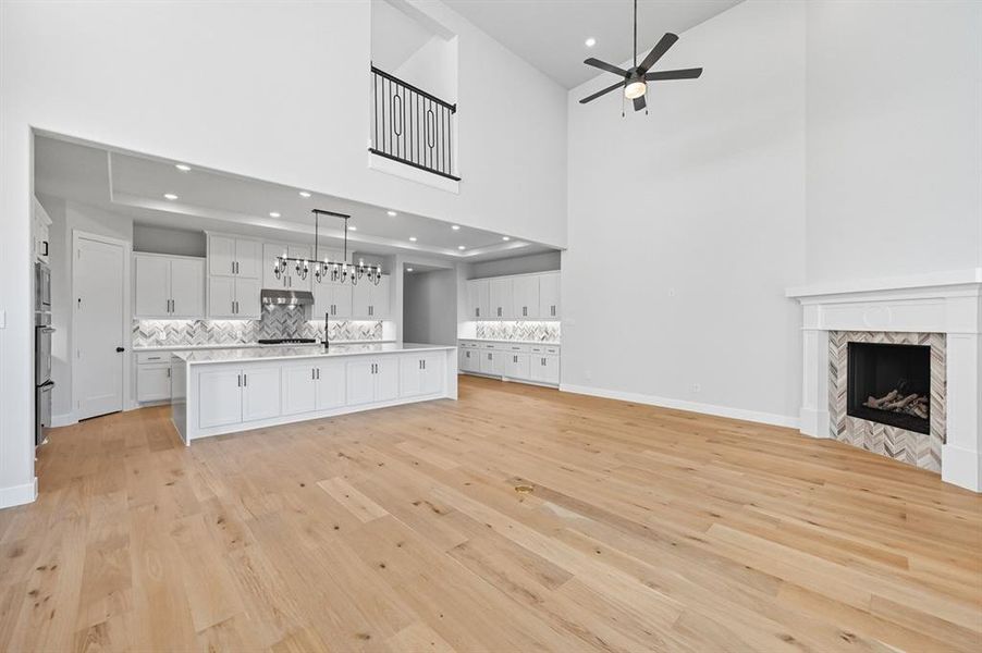 Unfurnished living room with a tile fireplace, light wood-style flooring, a high ceiling, recessed lighting, and ceiling fan