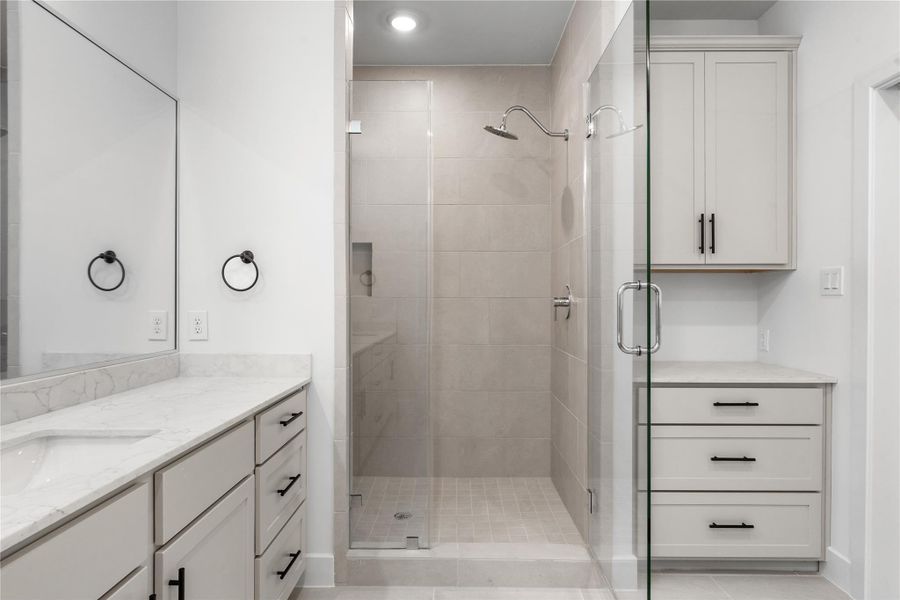 Custom primary shower & vanity — large-format tile surround, rain showerhead, grey shaker vanity with quartz counter, and built-in linen storage tower.