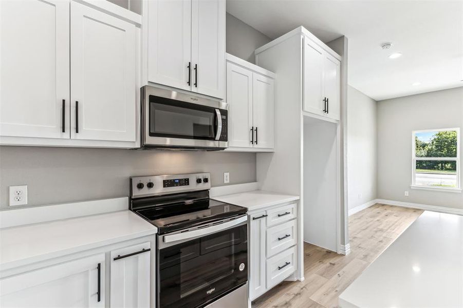 Kitchen with light wood-type flooring, appliances with stainless steel finishes, and white cabinetry