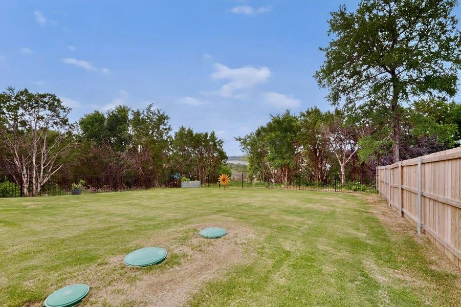 Expansive backyard featuring a manicured lawn, mature trees, and a wooden privacy fence