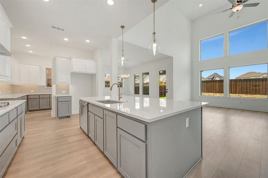 Kitchen featuring an expansive island with a built-in sink, stainless steel appliances, white upper cabinetry, and gray lower cabinetry Kitchen featuring an expansive island with a built-in sink, stainless steel appliances, white upper cabinetry, and gray lower cabinetry